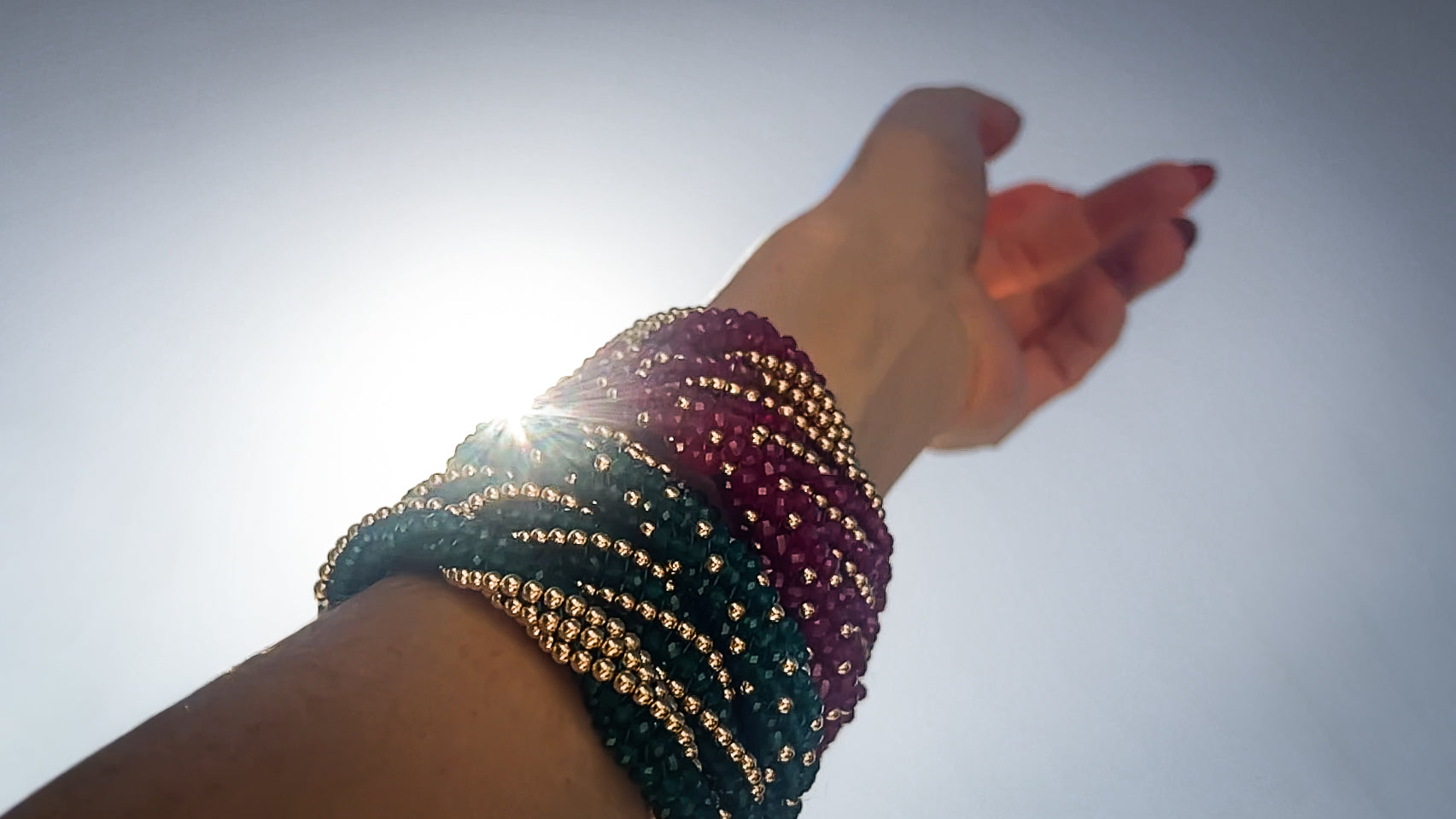 Hand wearing multiple beaded bracelets against a clear sky